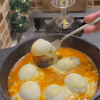 A Turkish breakfast skillet with halved boiled eggs in tomato sauce topped with melted cheese.