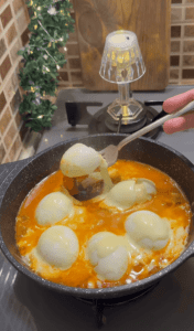 A Turkish breakfast skillet with halved boiled eggs in tomato sauce topped with melted cheese.