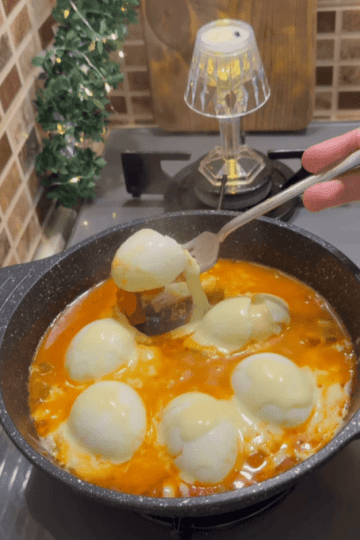 A Turkish breakfast skillet with halved boiled eggs in tomato sauce topped with melted cheese.
