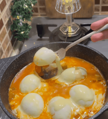 A Turkish breakfast skillet with halved boiled eggs in tomato sauce topped with melted cheese.