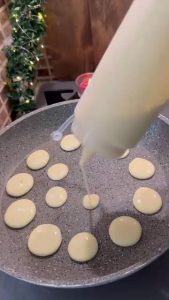 Transferring a heap of mini pancakes into a serving bowl.