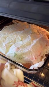 Pouring sauce over the peppers and covering the dish with a piece of wet, crumpled parchment paper.