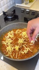 Sprinkling a generous amount of shredded kashar cheese over the skillet.