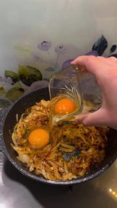 Cracking two fresh eggs over a bed of seasoned caramelized onions in the pan.