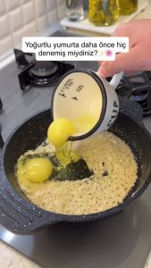 Cracking two large eggs over the golden, sautéed yogurt crumbles in the pan.