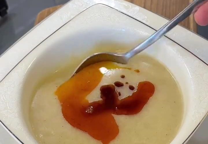 A bowl of silky blended potato and cornmeal soup topped with red pepper butter.