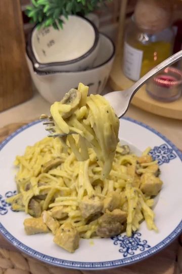 A plate of creamy golden curry chicken and mushroom pasta garnished with basil.