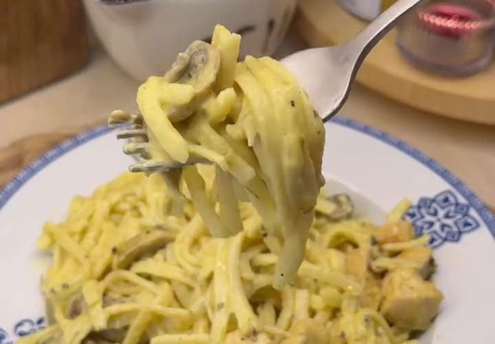 A plate of creamy golden curry chicken and mushroom pasta garnished with basil.