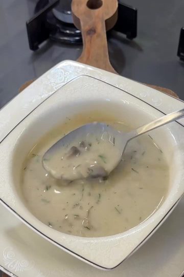 A bowl of creamy mushroom soup garnished with fresh dill and black pepper.