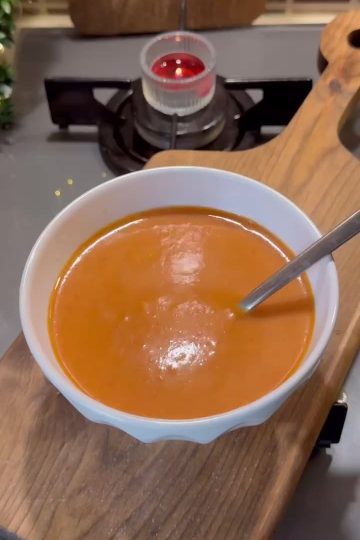 A bowl of vibrant red roasted capia pepper soup topped with cream and herbs.