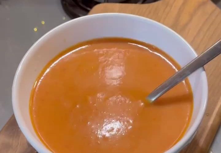 A bowl of vibrant red roasted capia pepper soup topped with cream and herbs.