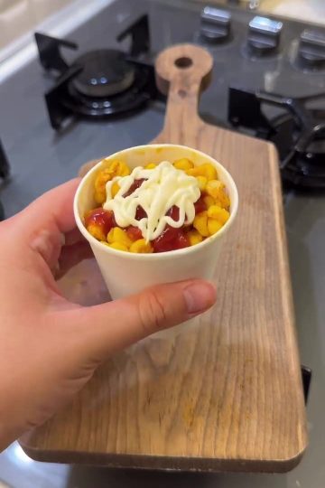 A cup of buttery Turkish street corn topped with ketchup and mayonnaise.