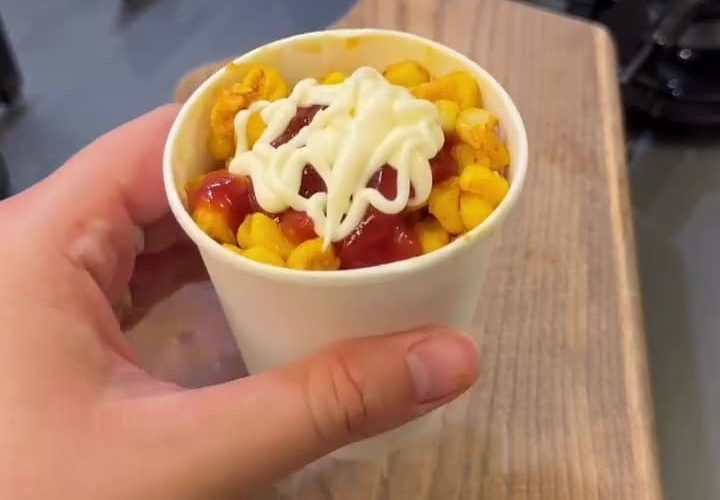 A cup of buttery Turkish street corn topped with ketchup and mayonnaise.