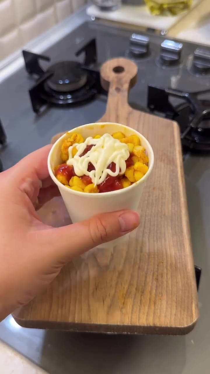 A cup of buttery Turkish street corn topped with ketchup and mayonnaise.