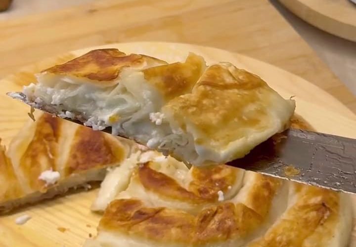 Two golden brown rose-shaped Turkish cheese pastries frying in a pan.