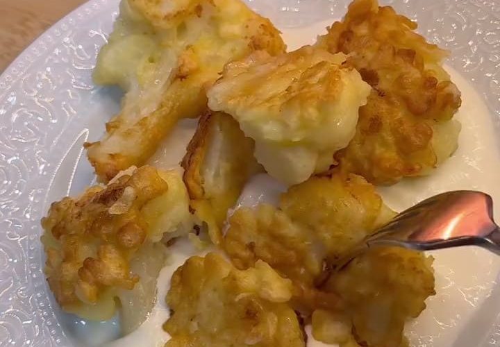 Golden brown crispy fried cauliflower florets served on a plate with a bowl of garlic yogurt.