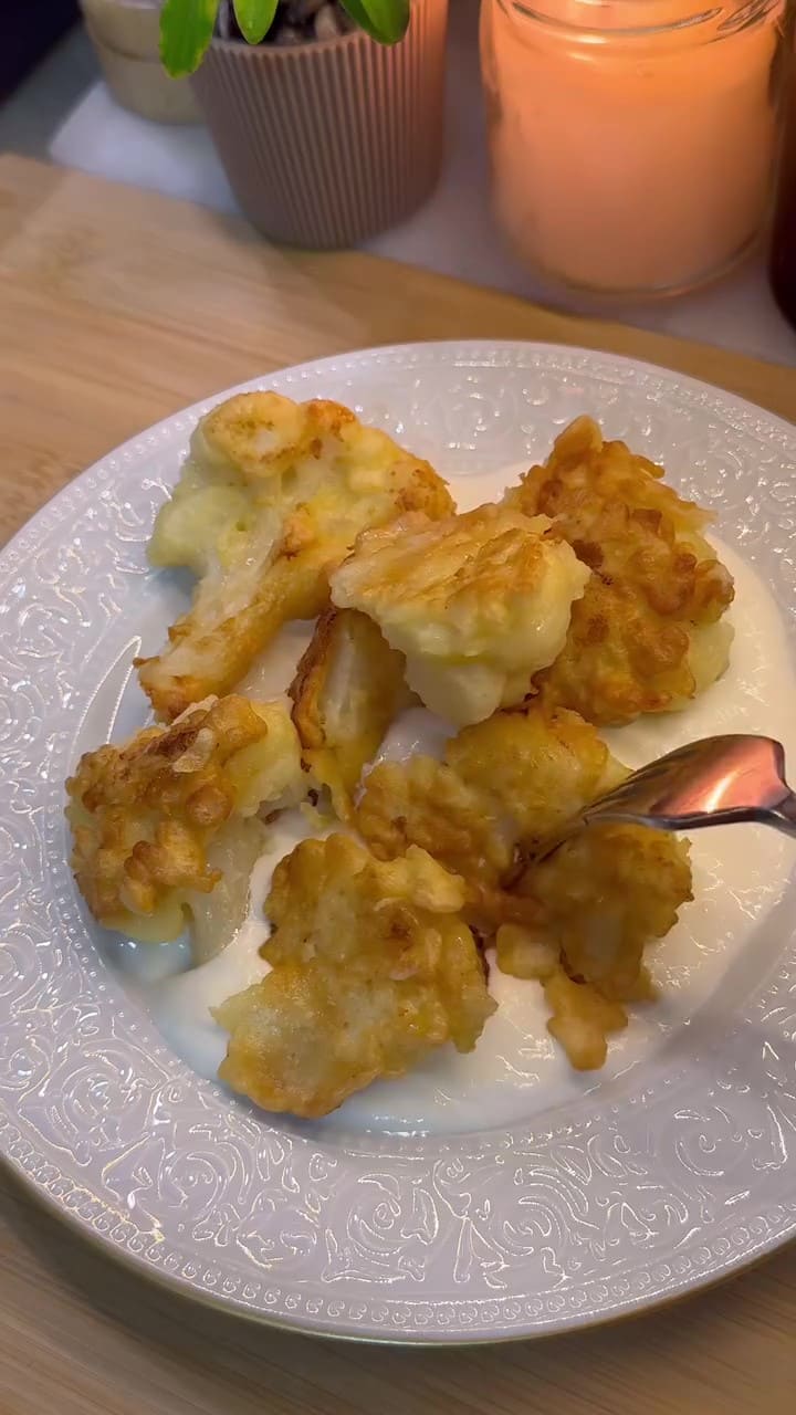 Golden brown crispy fried cauliflower florets served on a plate with a bowl of garlic yogurt.