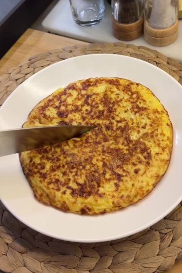 A golden brown, crispy potato omelet cut into wedges on a serving plate.