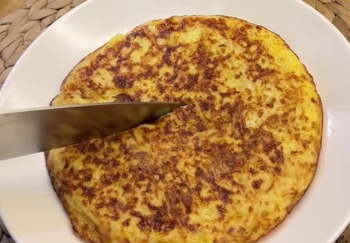 A golden brown, crispy potato omelet cut into wedges on a serving plate.