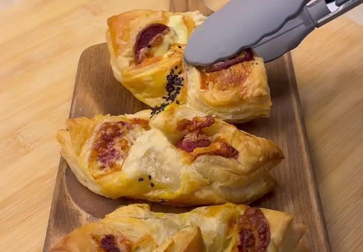 Golden brown crispy puff pastry bites filled with Turkish sucuk and melted cheese on a serving tray.