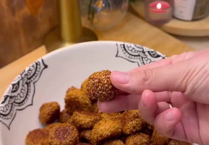A close-up shot of golden-brown crunchy Turkish sesame bite cookies (Lokmalık Susamlı Kurabiye) served on a plate with a traditional glass of Turkish tea.