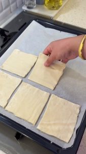 Slicing thawed puff pastry sheets into equal rectangular pieces for mini pizzas.