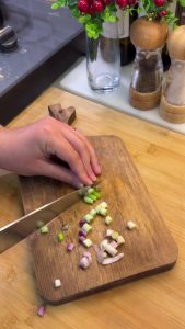 Dicing peeled hard-boiled eggs into small, even cubes on a cutting board.