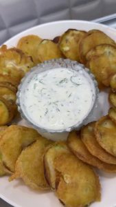 The final presentation of ultra-crispy fried zucchini slices served with a side of yogurt dip.