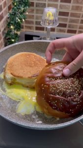 Flipping the cooked egg and hamburger bun over in a frying pan.