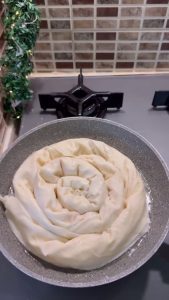 Flipping the börek in the pan to show the crispy golden brown underside.