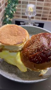 Folding the excess cooked egg inward onto the toasted hamburger bun.