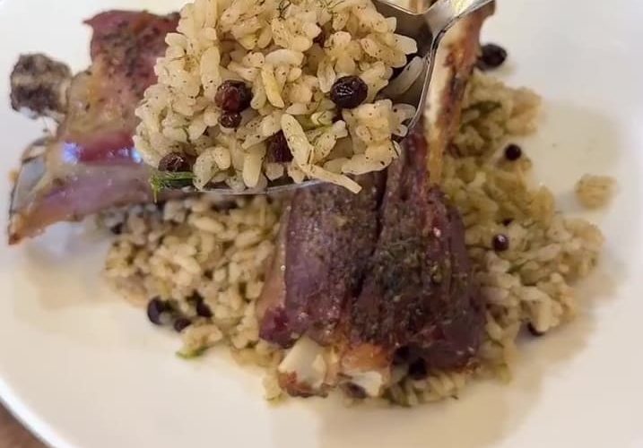 A close-up of fluffy Turkish aromatic rice pilaf garnished with fresh dill and currants.