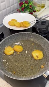 Frying the battered zucchini slices in hot bubbling oil until they turn golden yellow.