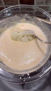 Frying batter-coated cauliflower florets in a pan with hot vegetable oil.