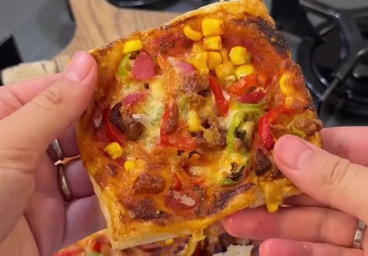 A baking tray filled with golden brown puff pastry mini pizzas topped with sucuk and cheese.