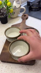 Greasing small ceramic ramekins with butter for the soufflé cakes.