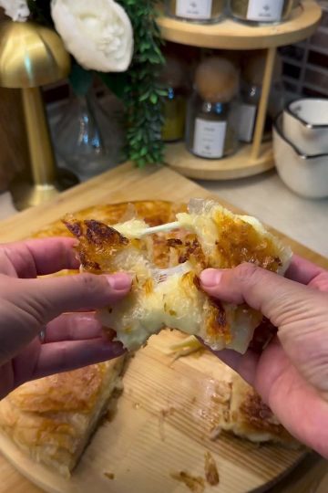 A close-up shot of a golden-brown, crispy square of Adana Böreği with a long, stretchy cheese pull served on a rustic plate.