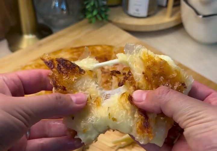 A close-up shot of a golden-brown, crispy square of Adana Böreği with a long, stretchy cheese pull served on a rustic plate.