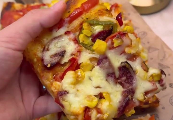 A large tray of freshly baked homemade Turkish pizza with sucuk, peppers, and melted kashar cheese.