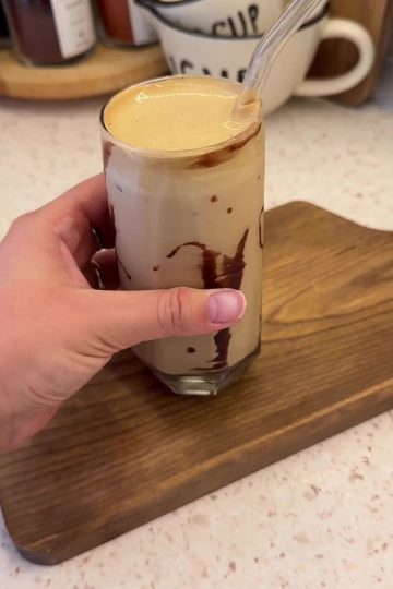 A tall glass of iced milk topped with thick honey whipped coffee foam.