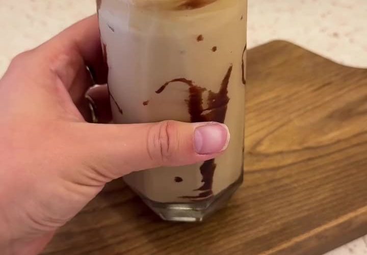 A tall glass of iced milk topped with thick honey whipped coffee foam.