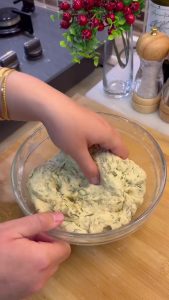 Gradually adding flour and kneading the soft dill pastry dough until smooth.