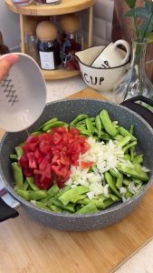 Adding chopped onions and peeled tomatoes over green beans in a large cooking pot.