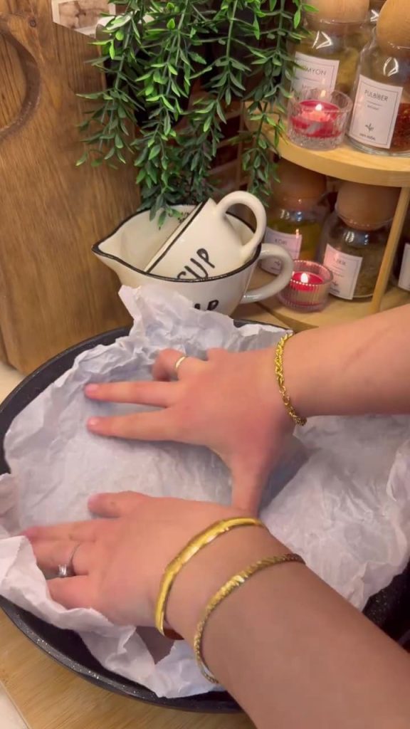 Lining a wide frying pan with a sheet of white parchment paper.