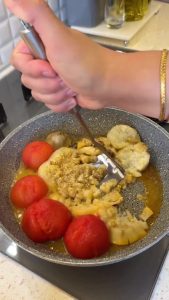 Mashing the softened tomatoes in the skillet to create a thick sauce.