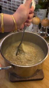 Mashing the cooked wheat grains vigorously with a potato masher to create a creamy texture.