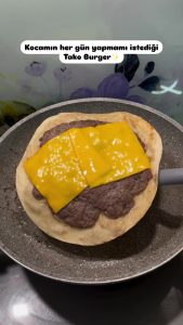 Using a glass lid to steam and melt the cheddar cheese on the smash taco burger.
