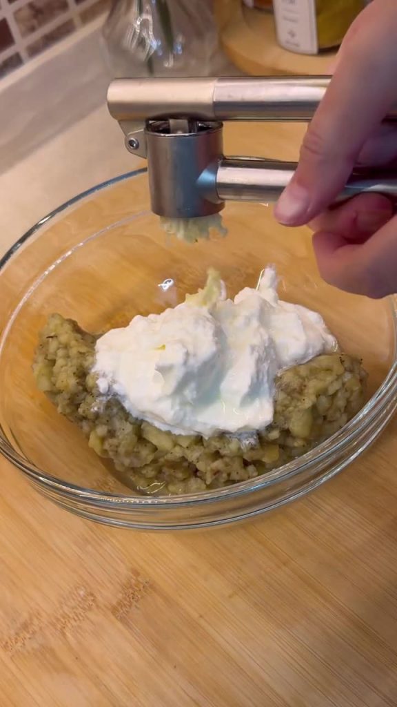 Whisking mashed roasted eggplant with thick garlic yogurt and salt.