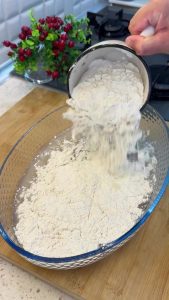 Mixing flour, dry yeast, and water in a large bowl using a spoon for no-knead bread.