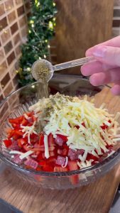Mixing diced sucuk, kashar cheese, tomatoes, and oregano in a glass bowl.